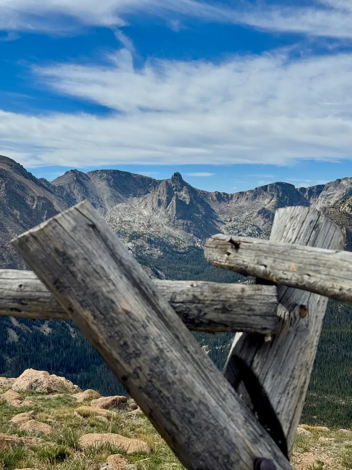 A weathered wooden fence overlooking a pine-covered valley and rocky peaks