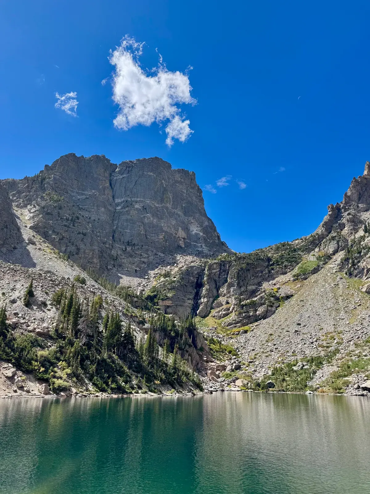 A turquoise alpine lake below steep rocky cliffs and a blue sky