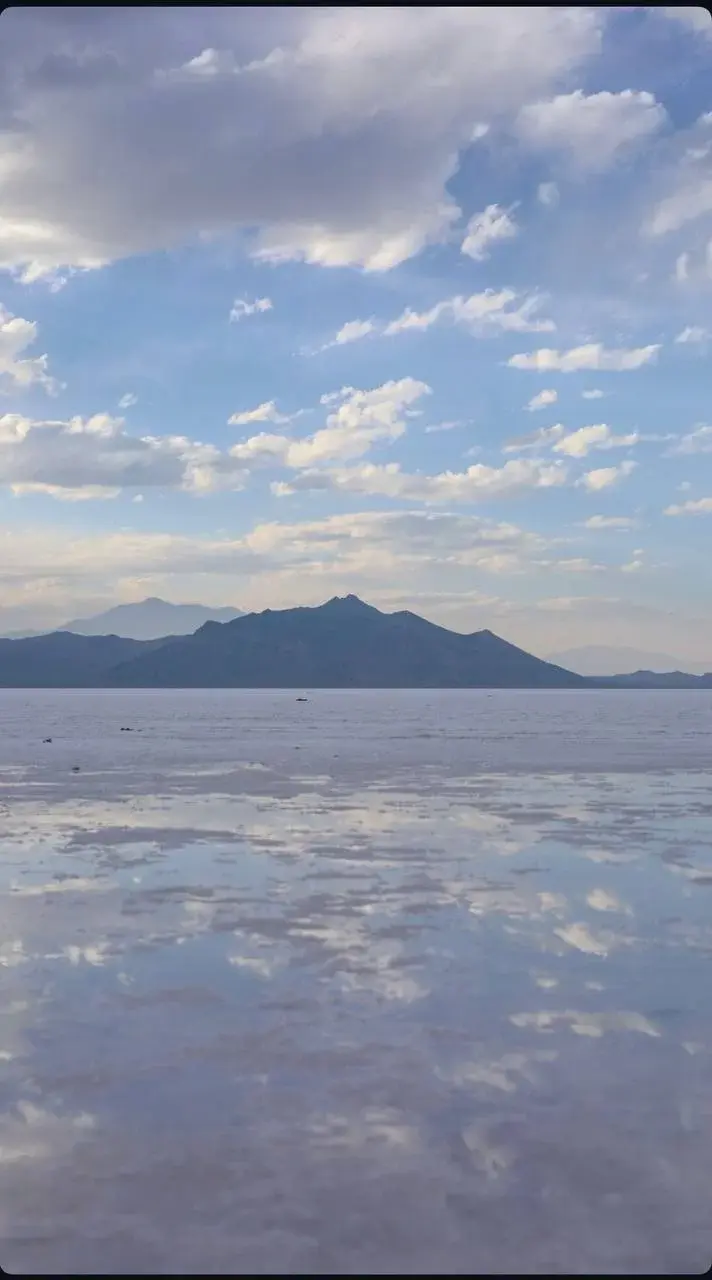 Distant mountain silhouettes and clouds reflected across a shallow sheet of water