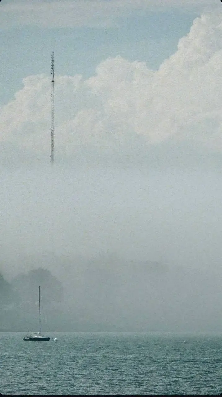 A lone sailboat on quiet water beneath a fog-covered shoreline